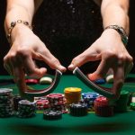 Hands holding playing cards over a green poker table.