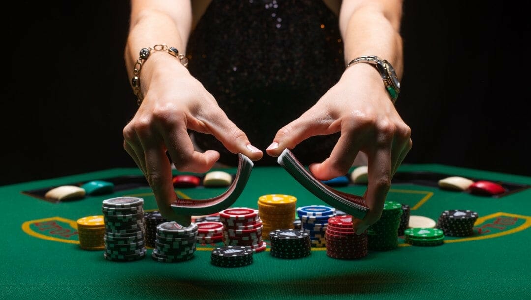 Hands holding playing cards over a green poker table.